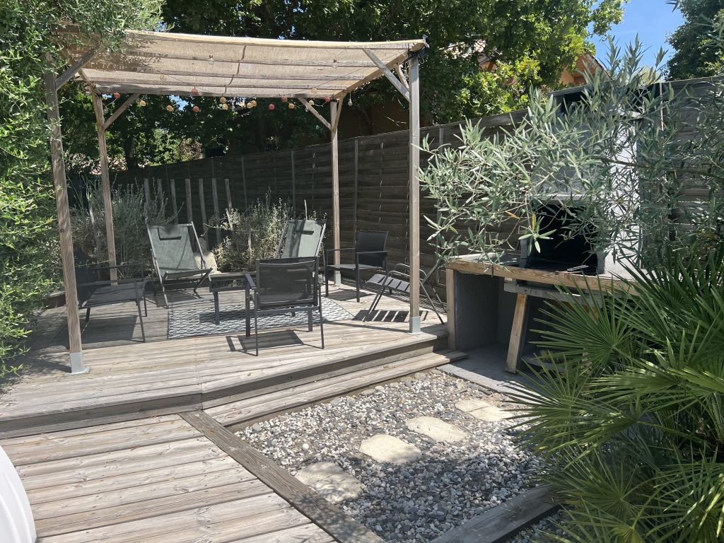 Terrasse extérieur avec accès au barbecue et au salon de jardin à côté.